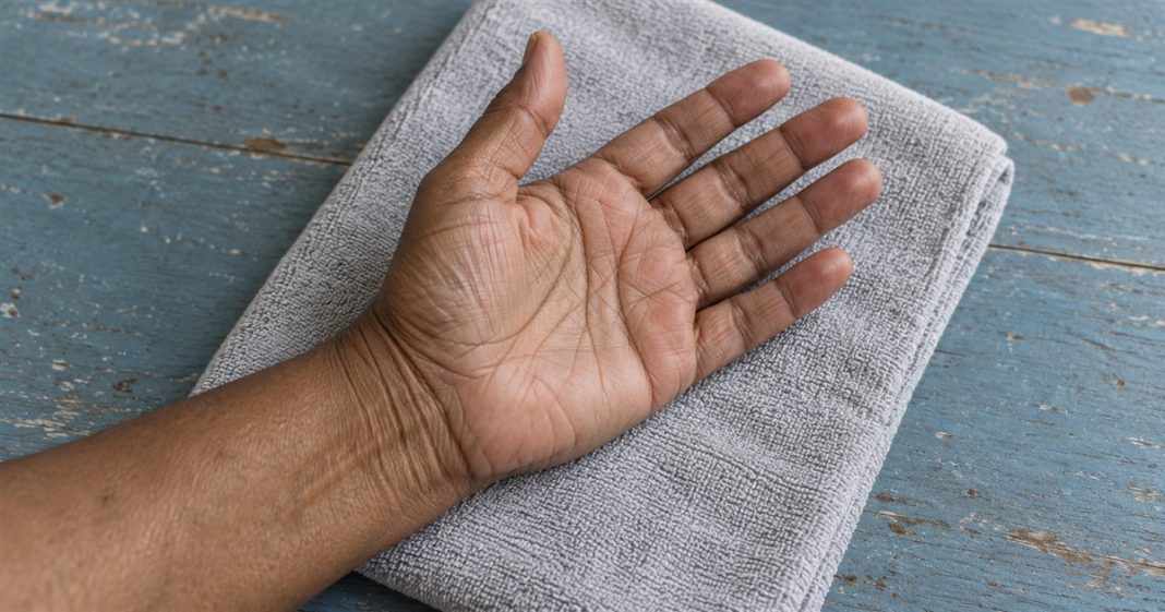 A relaxed open hand resting palm upward on a folded gray towel over a worn blue wooden table, with the thumb and fingers visible.