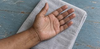A relaxed open hand resting palm upward on a folded gray towel over a worn blue wooden table, with the thumb and fingers visible.