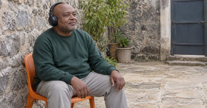 Empathy traits — courtyard headphone break 2687 A man wearing black headphones and a green sweatshirt seated on an orange chair in a stone courtyard.