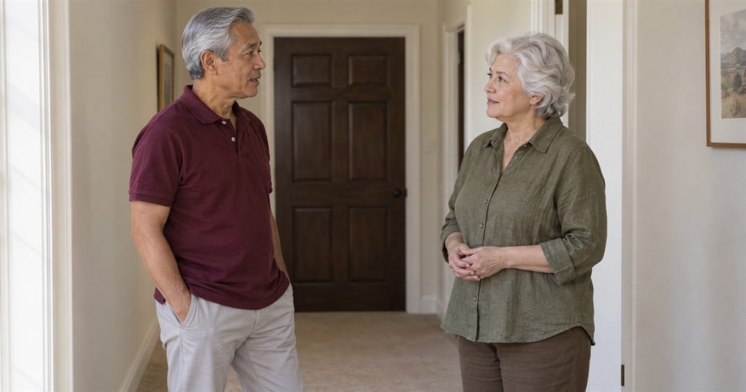 Two older adults standing apart and talking in a cream hallway near a closed dark-brown door.