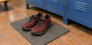 A pair of worn dark-red running shoes on a gray rubber mat beside blue gym lockers.