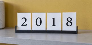 Four white cards displaying 2018 in a black holder on a gray shelf against a yellow wall.