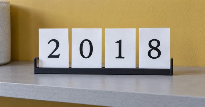2018 historical numerology: card display — realistic cover 20261005 Four white cards displaying 2018 in a black holder on a gray shelf against a yellow wall.