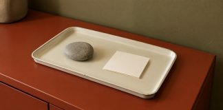 A smooth gray stone and a blank folded card on an ivory tray atop a red metal cabinet.