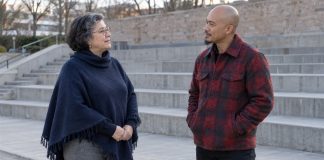 A woman in a navy poncho and a man in a red plaid jacket talking beside outdoor concrete seating steps.