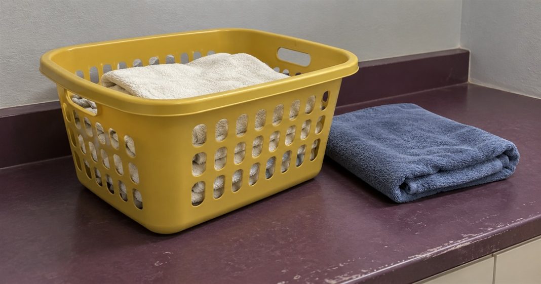Small laundry task — Everyday self-reliance A yellow laundry basket holding off-white towels beside a folded blue towel on a worn purple counter.