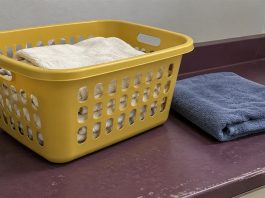 A yellow laundry basket holding off-white towels beside a folded blue towel on a worn purple counter.