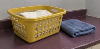 A yellow laundry basket holding off-white towels beside a folded blue towel on a worn purple counter.