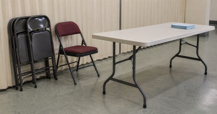 Community room setup — Ways of using available Chances Folded metal chairs beside a burgundy chair and an off-white folding table with blue sheets in a plain community room.
