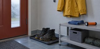 Worn black boots on a tray beside a metal shelf with folded blue knitwear and an orange flashlight, below a yellow jacket.