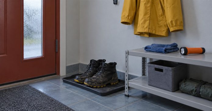 Worn black boots on a tray beside a metal shelf with folded blue knitwear and an orange flashlight, below a yellow jacket.