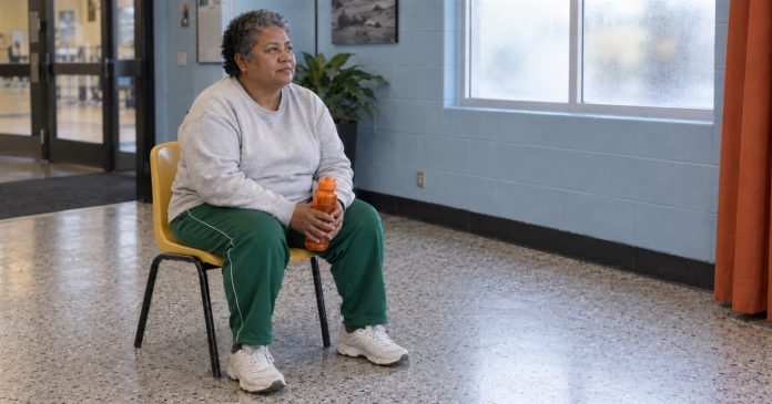 Photographic-style editorial image of a woman resting on a yellow chair with an orange water bottle in a quiet lobby.