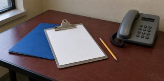 Gray corded telephone, blank clipboard, blue folder and pencil on a worn red-brown desk