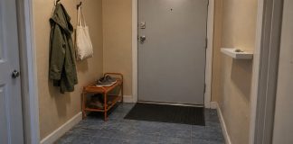 Modest apartment entryway with a gray door, orange shoe rack, coat, canvas bag and black doormat