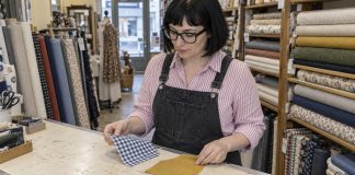 Woman in glasses and striped shirt comparing blue gingham and mustard fabric samples in a textile shop