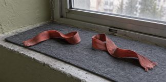 Two separate rust-red fabric ribbons rest on a gray felt mat on a worn windowsill.