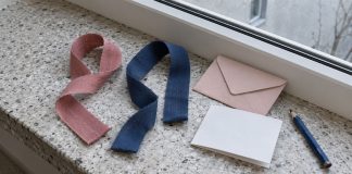 Separate rose and navy ribbons beside a pink envelope, blank note and blue pencil on a terrazzo windowsill.