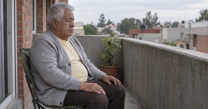 Prayer realistic balcony pause 3727 Man in a gray cardigan sitting with eyes closed and hands on his thighs on a concrete balcony.