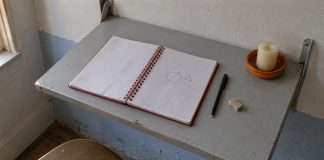 Open spiral notebook with a simple geometric sketch, pen and unlit candle on a gray metal shelf.