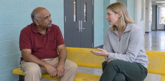 Man in a red polo listening to a woman in a gray sweatshirt on a yellow recreation-center bench.