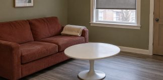 A modest living room with a brick-red sofa, folded blanket and cleared white coffee table.