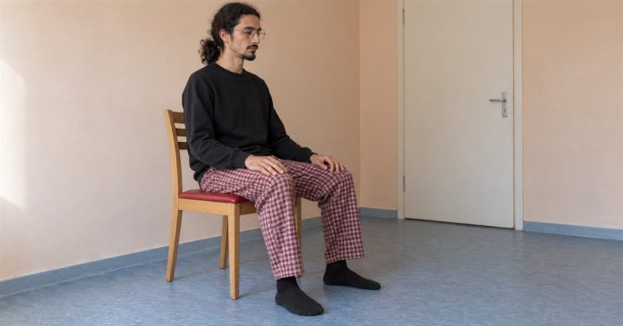 Psychic888 realistic ordinary seated meditation 3833 Man sitting quietly on a wooden chair with hands resting on his thighs and feet on the floor.