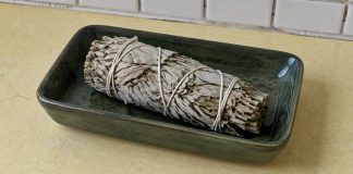 Unlit dried sage bundle in a dark-green ceramic dish on a pale-yellow kitchen counter.