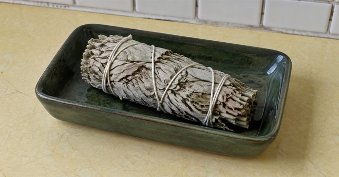 Psychic888 realistic unlit sage kitchen 3843 Unlit dried sage bundle in a dark-green ceramic dish on a pale-yellow kitchen counter.