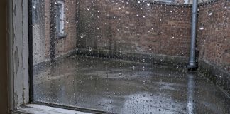 Raindrops on a closed window overlooking a wet brick-walled courtyard.