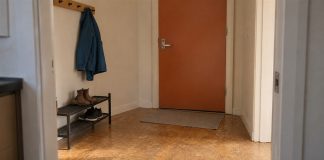 A clear home entryway with an orange door, a compact shoe rack and a blue coat on wall hooks.