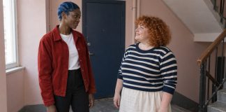 Two women having a warm conversation on an apartment landing beside a blue door.