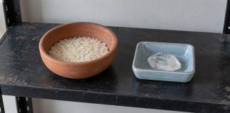 A terracotta bowl of dry rice beside a clear crystal in a separate blue dish on a black shelf.
