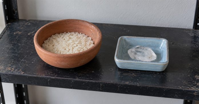 Psychic888 realistic separate rice crystal 3882 A terracotta bowl of dry rice beside a clear crystal in a separate blue dish on a black shelf.