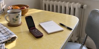 Burgundy flip phone beside a spiral notepad and black pen on a pale yellow kitchen table.