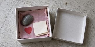 Open cardboard keepsake box with pink cloth, a smooth stone, red paper heart and folded note