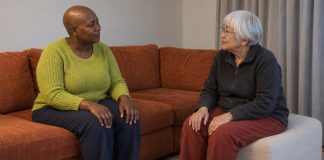 Two women having a quiet conversation beside an orange sofa and cream ottoman