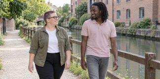 Two adults smiling toward each other while walking beside a canal and timber fence