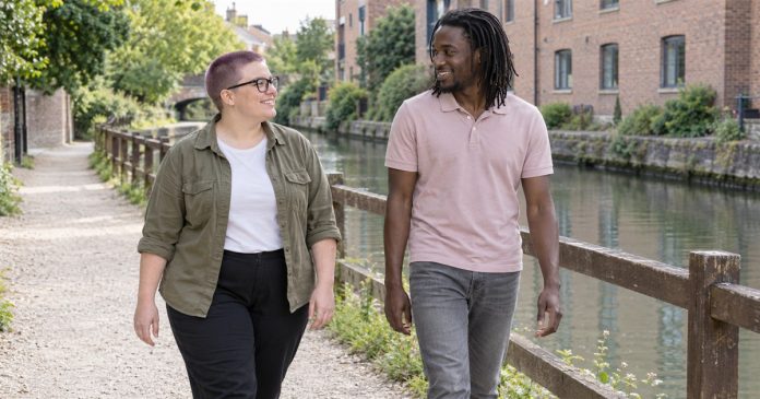 Right Relationship — Realistic Canal Conversation Two adults smiling toward each other while walking beside a canal and timber fence