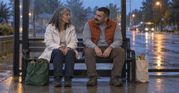 Two adults talking on a bus-stop bench at dusk with grocery bags beside them