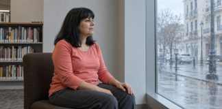 A woman in a coral top taking a quiet pause beside a rainy library window