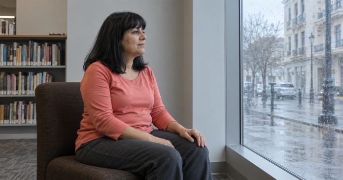 A woman in a coral top taking a quiet pause beside a rainy library window