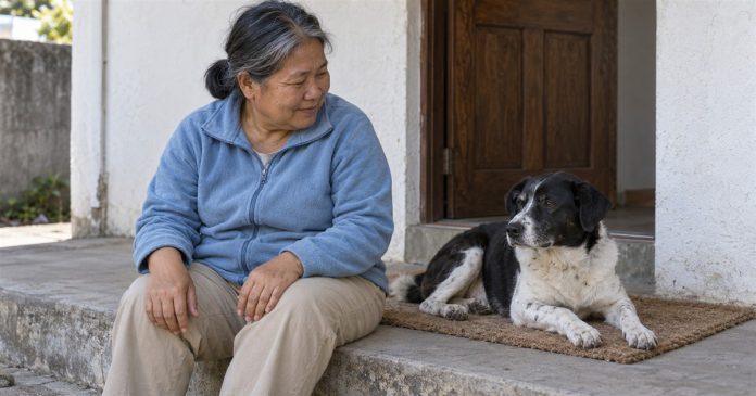 A woman in a blue fleece sitting on a concrete step beside a relaxed black-and-white dog