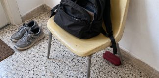 A black backpack on a yellow chair with a red glasses case partly tucked behind a chair leg