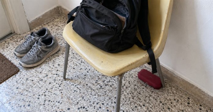 Realistic misplaced case 3995 A black backpack on a yellow chair with a red glasses case partly tucked behind a chair leg