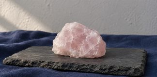 A rough pale-pink rose-quartz stone on a dark slate slab with navy cloth