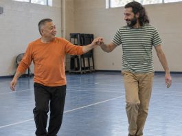 Two men smiling while practicing a dance step together in a recreation-center gym