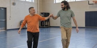 Two men smiling while practicing a dance step together in a recreation-center gym