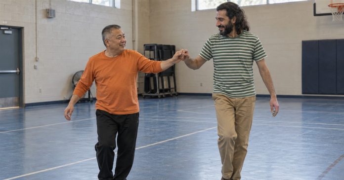 Two men smiling while practicing a dance step together in a recreation-center gym