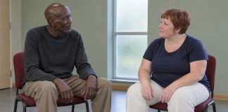 A man and woman seated on separate red chairs in attentive conversation