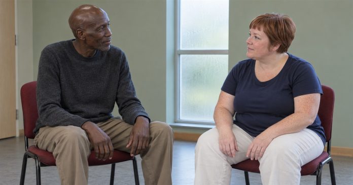 A man and woman seated on separate red chairs in attentive conversation